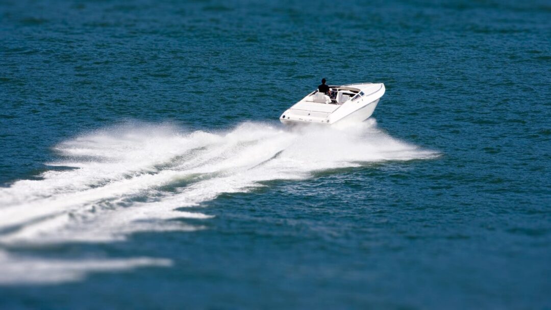 Small white speedboat leaving foamy wake on blue water